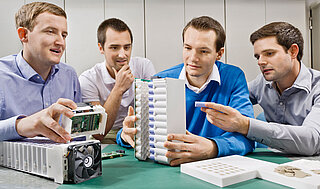 The 4 company founders of INVENOX sit at the table and examine a battery system.