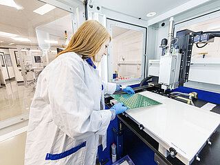 A woman checks an INVENOX module circuit board fitted with contacting material