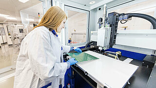 A woman checks an INVENOX module circuit board fitted with contacting material
